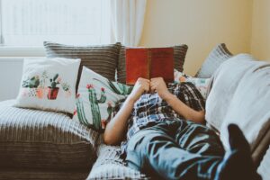 A person laying on the sofa reading a book